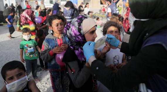 Eine Frau hilft einem Kind in einem Flüchtlingslager in Idlib eine Schutzmaske aufzusetzen.