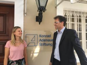 Laura Hermsdorf und Jan Woischnik vor dem KAS Logo im Büro in Rio
