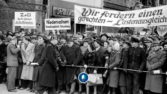 Schwarz-weiss Bild. Menschenmenge vor einem Gebäude mit Schildern 'Niedersachsen Verwaltungsbezirk Braunschweig' und 'Wir fordern einen gerechten Lastenausgleich'.