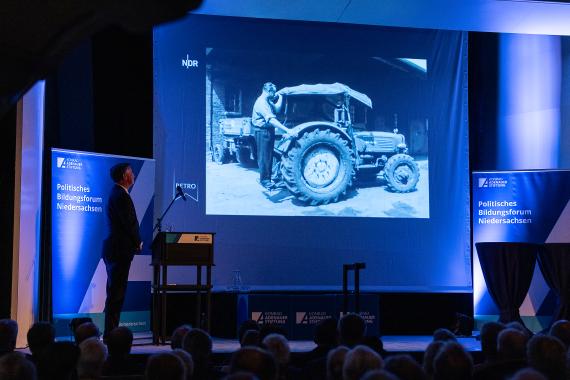 Fotografie der Veranstaltung vom Politischen Bildungsforum Niedersachsen. Zu sehen eine blau beleuchtet Bühne mit einer Präsentation.