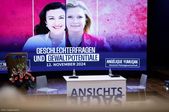Zwei Personen vor einer Wand mit Text 'GESCHLECHTERFRAGEN UND GEWALTPOTENTIALE 12. NOVEMBER 2024 ANGÉLIQUE YUMUSAK Deutsche Polizeigewerkschaft'