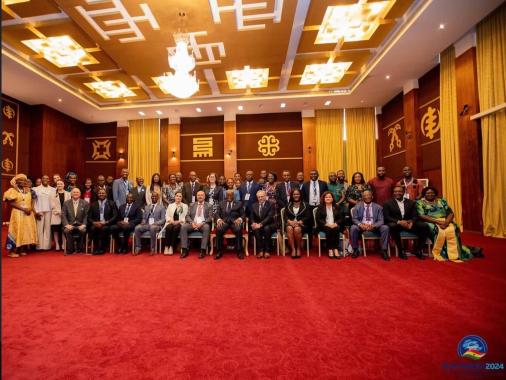 Menschen in formeller Kleidung in einem Saal mit roten Teppich und goldfarbenen Vorhängen, die für ein Gruppenfoto posieren