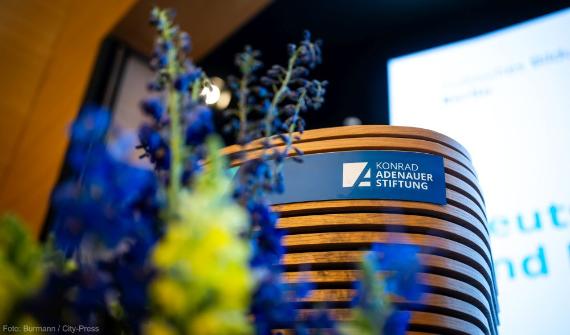 Blaue Blumen, das Logo der Konrad-Adenauer-Stiftung dahinter auf einem Rednerpult in der Akademie.