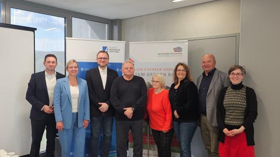 Gruppe von acht Personen steht vor zwei aufgestellten Roll-ups in einem Büroraum