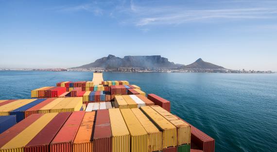 Großes Containerschiff verlässt den Hafen von Kapstadt mit dem Tafelberg und der Stadt im Hintergrund, Südafrika. Sicht vom Brückendeck eines Containerschiffs, das Kapstadt verlässt, mit Blick zurück auf die Stadt.
