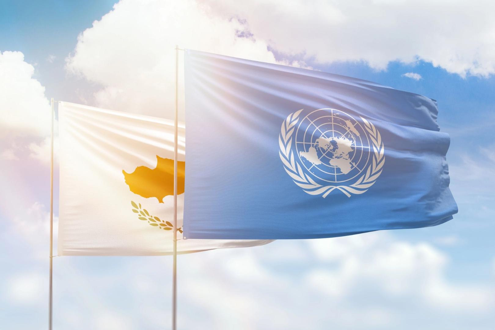 Flaggen der Vereinten Nationen und Zyperns wehen auf Fahnenmasten vor blauem Himmel mit Wolken