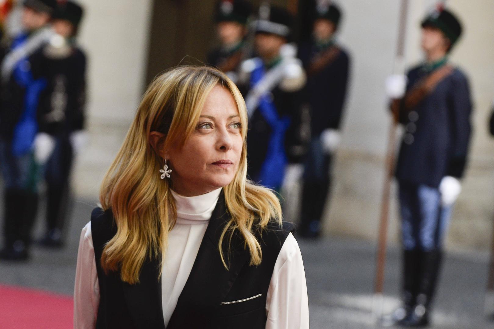 Giorgia Meloni steht vor uniformierten Ehrenwachen bei einer Zeremonie im Freien.