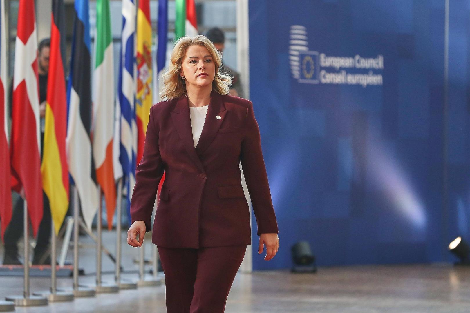 Frau in dunkelrotem Hosenanzug geht vor einer Reihe von Flaggen und einem Schild mit der Aufschrift 'European Council Conseil européen'