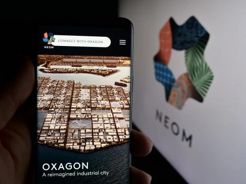 Person holding smartphone with web page of Saudi Arabian real estate project NEOM on screen in front of logo