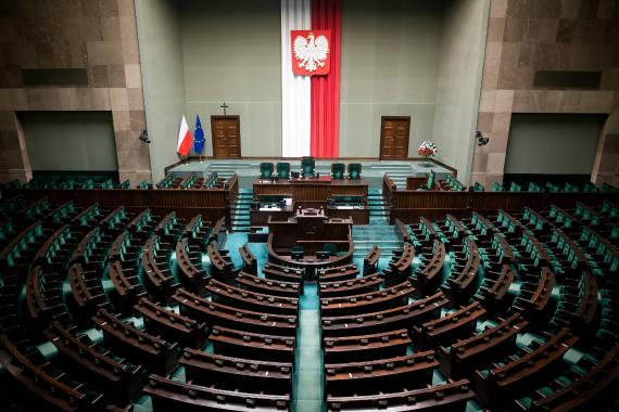 Halbrunder Plenarsaal mit Reihen von Sitzplätzen und Podium vor Wand mit polnischer Flagge und Wappen