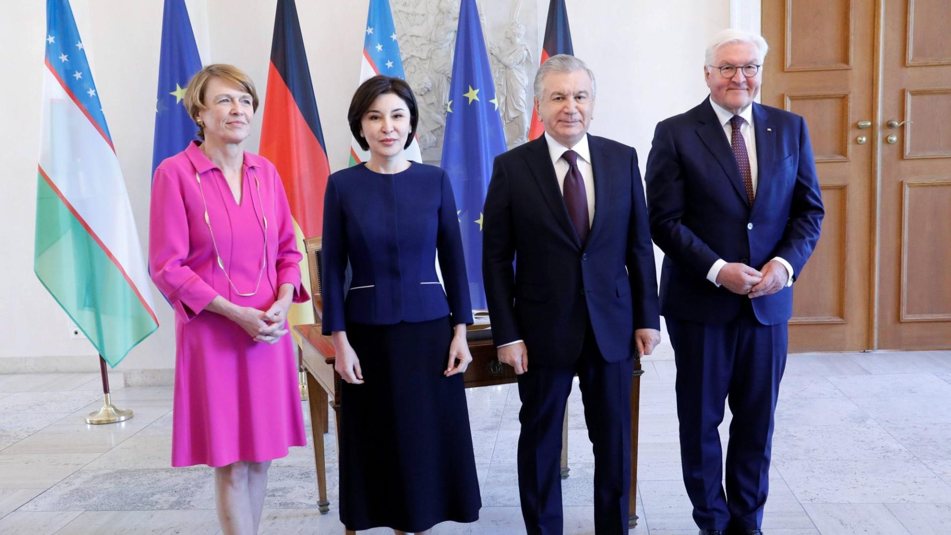 Vier Personen in formeller Kleidung stehen nebeneinander vor den Flaggen von Usbekistan, Deutschland und der Europäischen Union in einem repräsentativen Raum