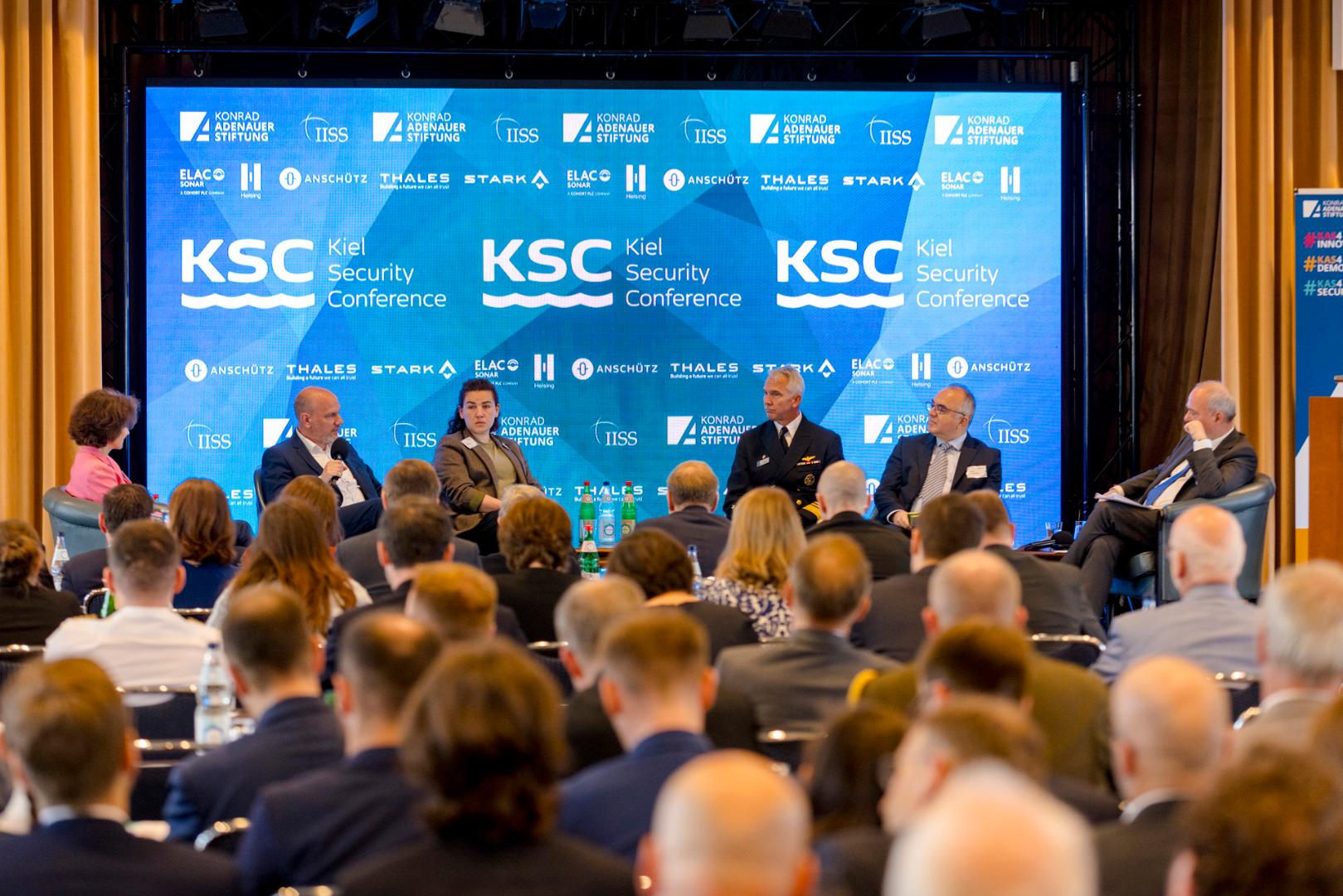 Podiumsdiskussion mit sechs Personen vor großem Bildschirm mit Logos und Schriftzug 