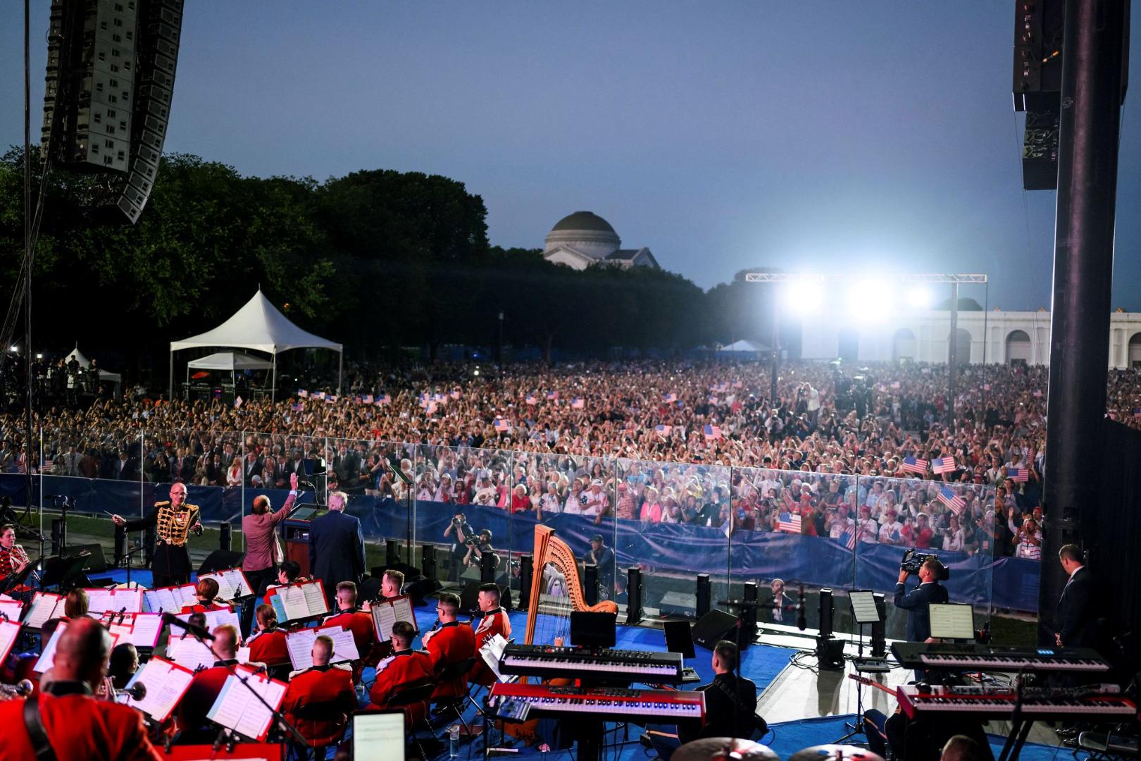 Blick von der Bühne auf ein großes Publikum bei einer abendlichen Veranstaltung mit Orchester im Vordergrund und hellen Scheinwerfern im Hintergrund